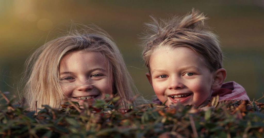 children-1879907-1200x628-5d150347297bf Two young girls peeking up from behind a bush