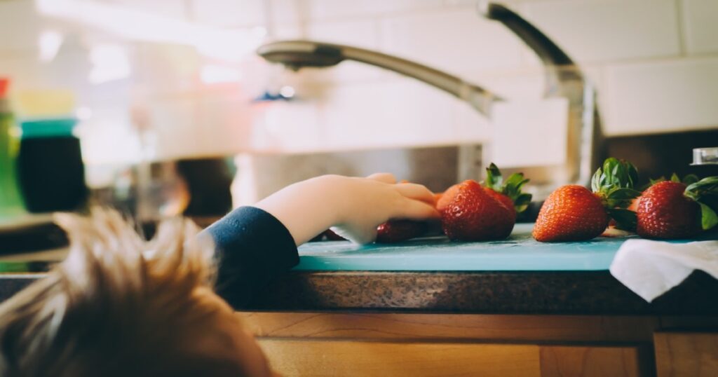 photo-1487795924438-1200x630-5e68fd85cb01f Young child reaching for strawberries on a countertop